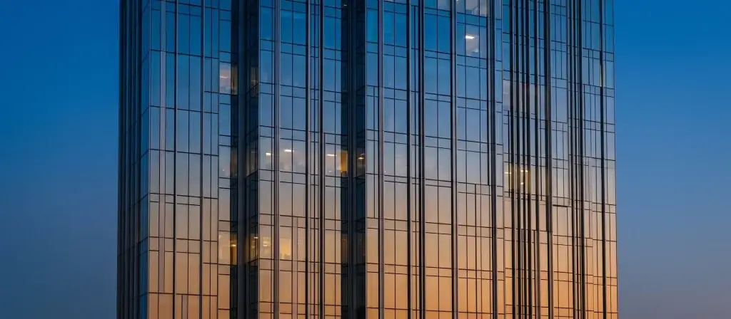 Fachada acristalada de un edificio de oficinas del distrito financiero al anochecer, con reflejos del cielo, ilustrativa de la financiación institucional del sector