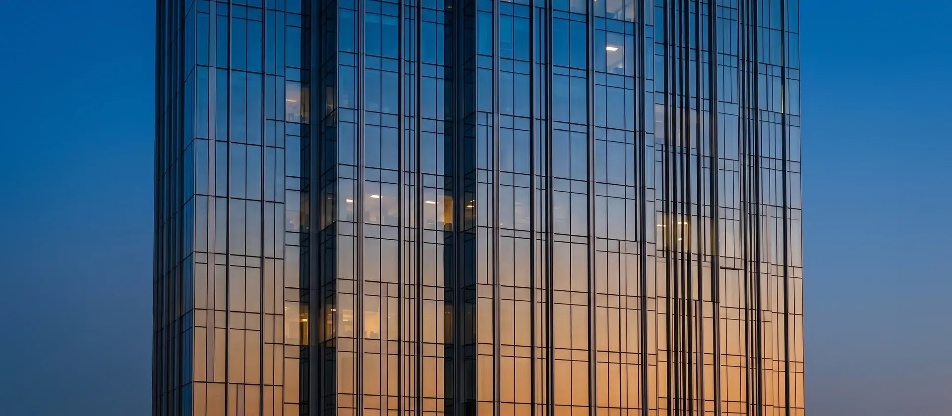 Fachada acristalada de un edificio de oficinas del distrito financiero al anochecer, con reflejos del cielo, ilustrativa de la financiación institucional del sector