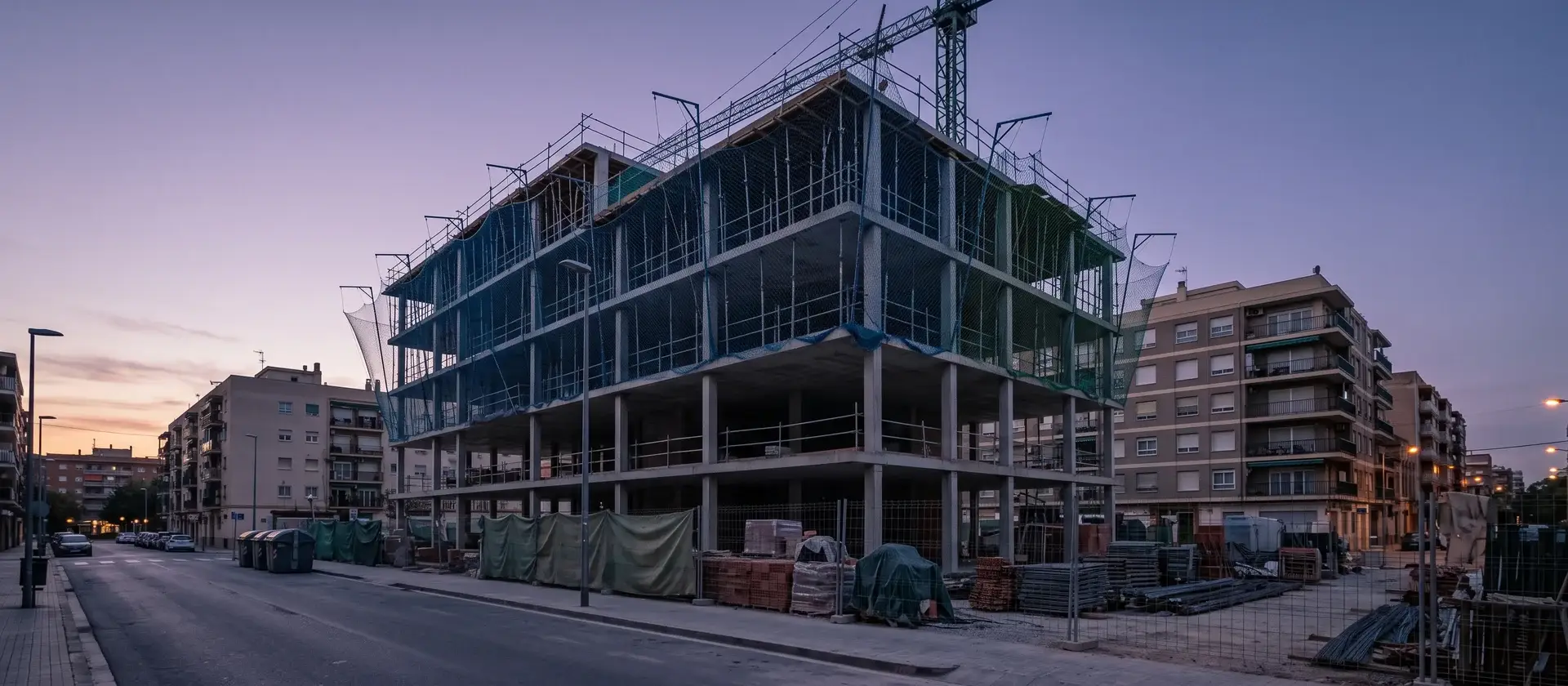 Edificio de alojamiento flexible en construcción con grúa y andamios en una ciudad española al atardecer, imagen ilustrativa del freno de las inversiones
